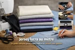 Photo horizontale d’un atelier couture avec machine à coudre, piles de tissus jersey et lycra, patron et accessoires, pour illustrer un guide sur le jersey lycra au mètre.