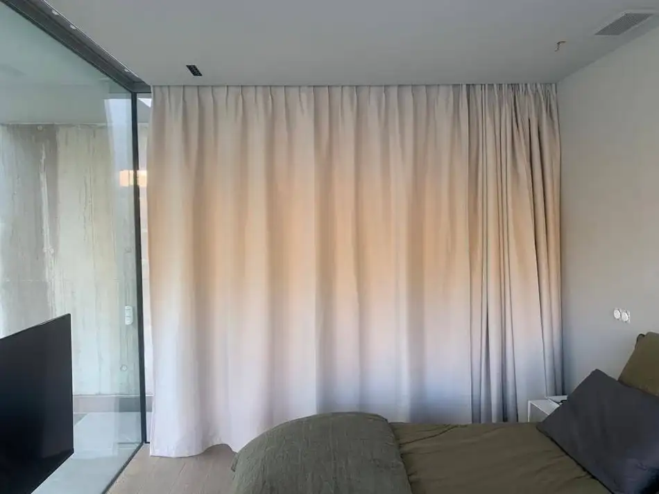 Rideaux en tissu d’ameublement clair installés dans une chambre, idéals pour habiller une fenêtre et créer une ambiance douce et élégante